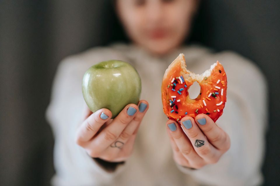 Woman with a lack of willpower not sticking to her diet and eating a donut instead