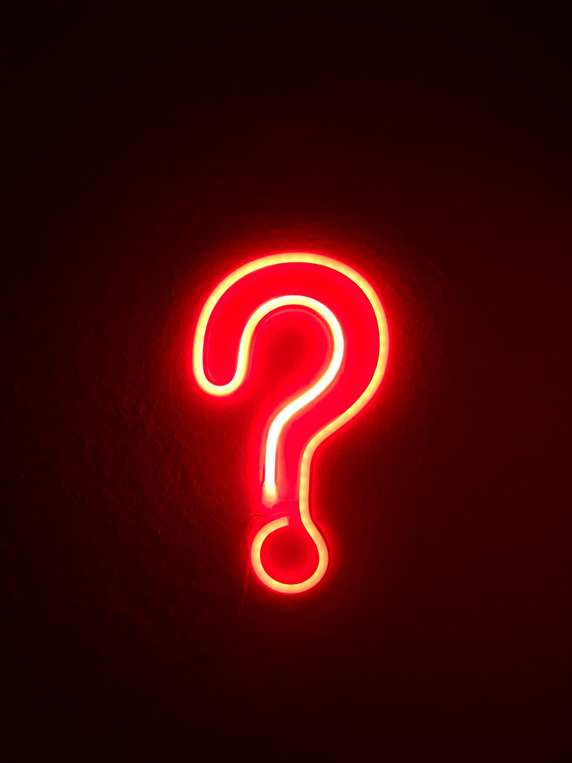 Image of a red neon light in the shape of a question mark.