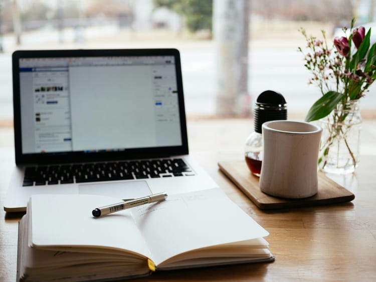 Image of a laptop, book and pen, and a coffee mug. 